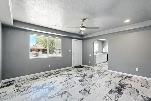unfurnished room with a ceiling fan, a sink, arched walkways, baseboards, and a textured ceiling