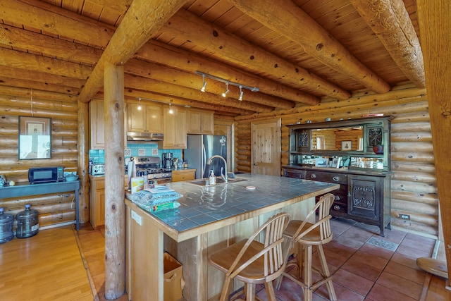 387 County Rd B64, Pecos, NM 87552 - kitchen featuring tile countertops, stainless steel appliances, under cabinet range hood, beamed ceiling, and rustic walls