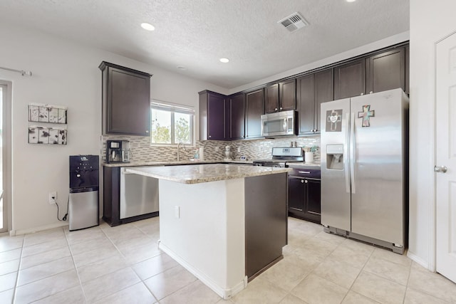 7105 Napoleon Rd NE, Rio Rancho, NM 87144 - kitchen with stainless steel appliances, backsplash, dark brown cabinetry, a textured ceiling, and a center island