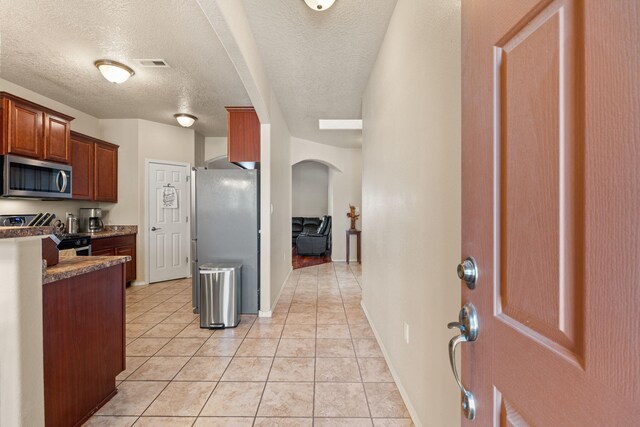 5668 Cold Creek Ave NW, Albuquerque, NM 87114 - kitchen featuring stainless steel appliances, light tile patterned flooring, dark countertops, a textured ceiling, and arched walkways