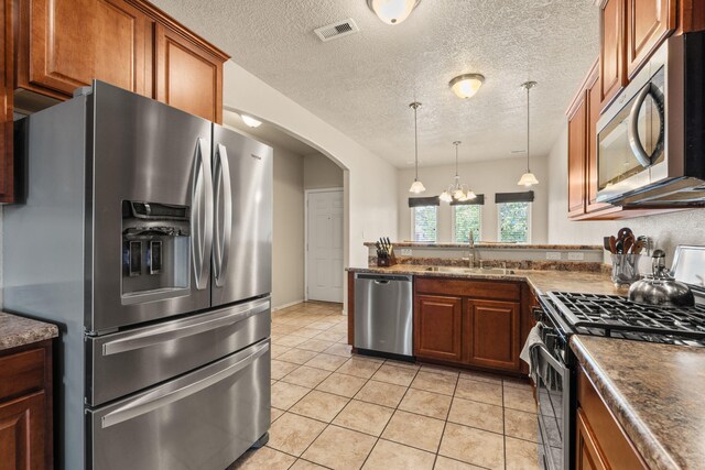 5668 Cold Creek Ave NW, Albuquerque, NM 87114 - kitchen with appliances with stainless steel finishes, a sink, brown cabinetry, a peninsula, and a textured ceiling