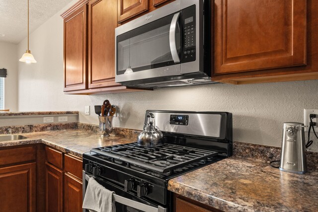 5668 Cold Creek Ave NW, Albuquerque, NM 87114 - kitchen featuring appliances with stainless steel finishes, dark countertops, a textured ceiling, decorative light fixtures, and brown cabinetry