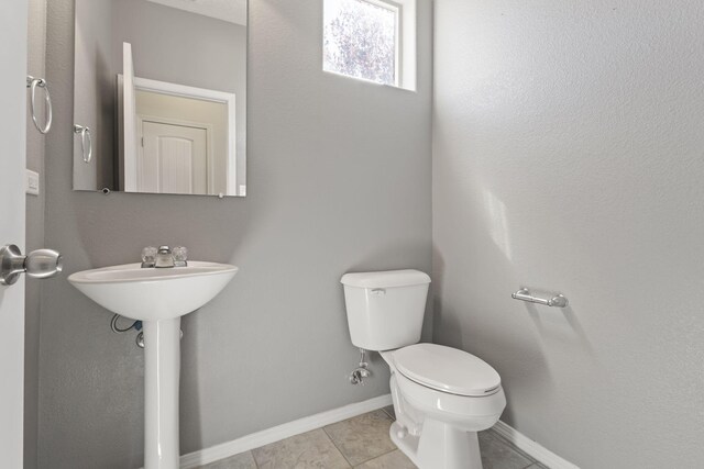 half bathroom with toilet, tile patterned flooring, and baseboards