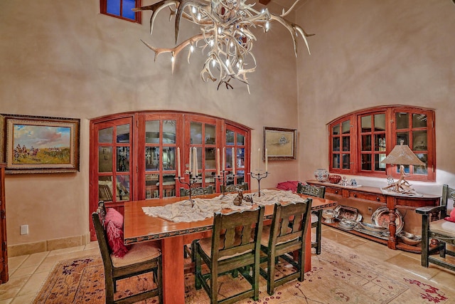 tiled dining space featuring a notable chandelier, french doors, and a towering ceiling