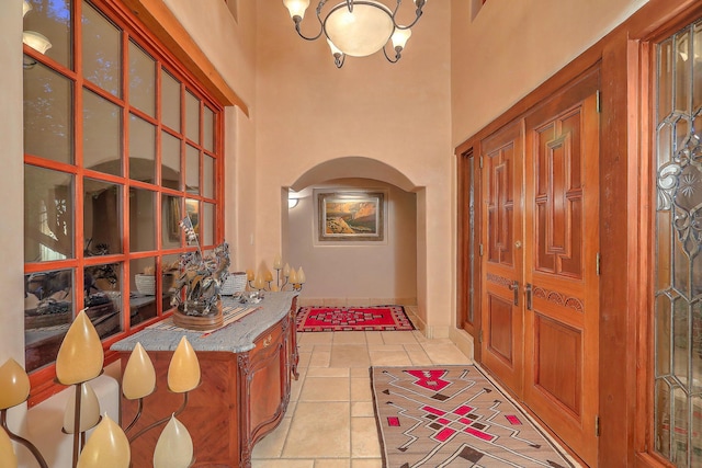foyer entrance featuring baseboards, a towering ceiling, arched walkways, and light tile patterned floors