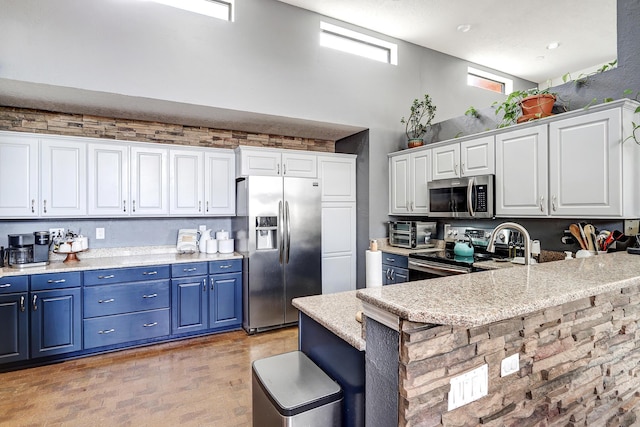 kitchen featuring blue cabinets, a breakfast bar area, stainless steel appliances, white cabinetry, and a peninsula