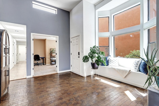 entrance foyer with a towering ceiling, brick floor, and baseboards