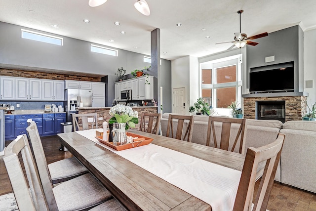 dining room featuring recessed lighting, wood finished floors, a fireplace, a ceiling fan, and a towering ceiling