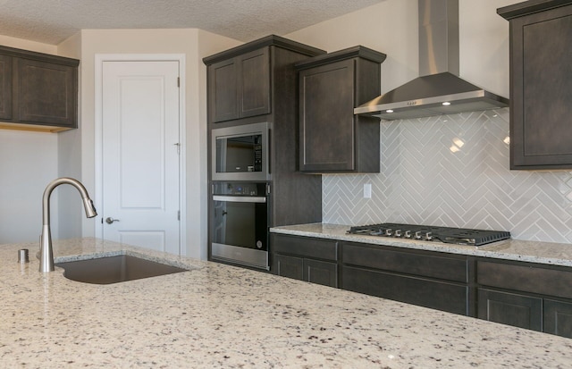 kitchen with wall chimney range hood, stainless steel appliances, a sink, and dark brown cabinetry