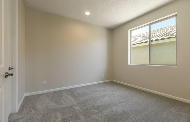 spare room with a textured ceiling, carpet floors, and baseboards