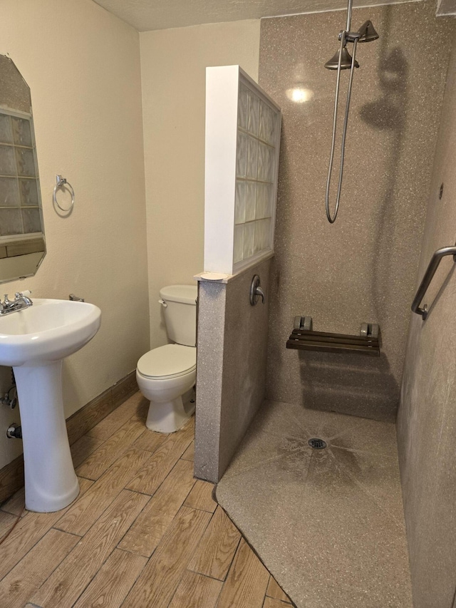 bathroom with a tile shower, wood finish floors, toilet, and a sink