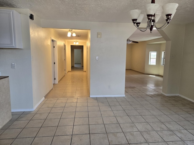 empty room featuring light tile patterned flooring, arched walkways, a textured ceiling, and an inviting chandelier