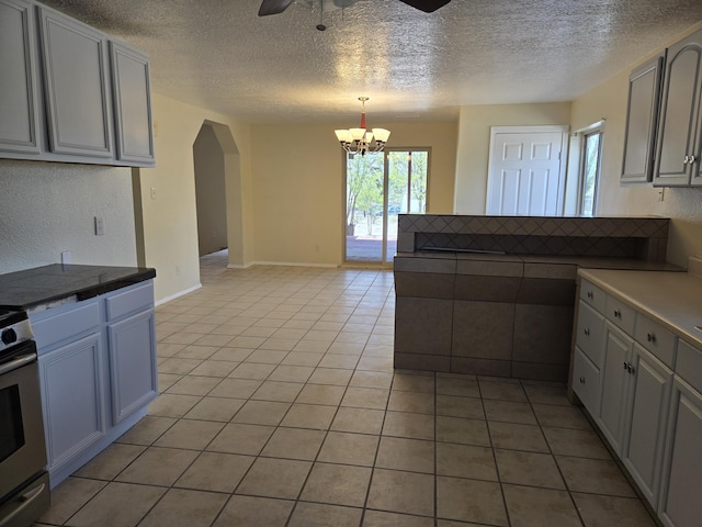 kitchen with electric stove, arched walkways, light tile patterned flooring, a textured ceiling, and ceiling fan with notable chandelier