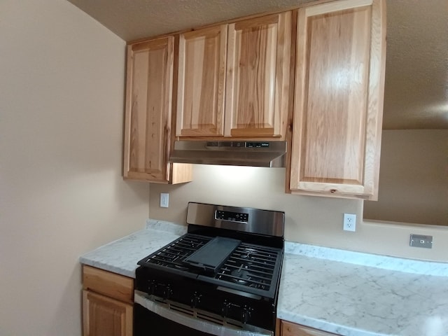 kitchen with gas range, under cabinet range hood, a textured ceiling, and light brown cabinetry
