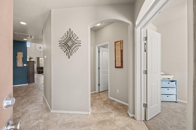 hallway featuring a textured ceiling, visible vents, baseboards, and arched walkways