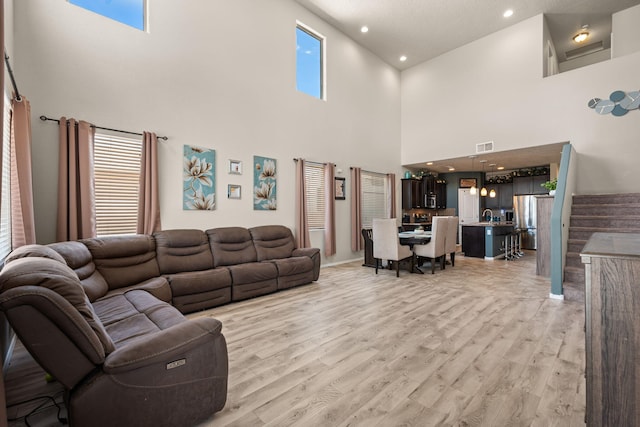 living area with visible vents, light wood-type flooring, recessed lighting, a towering ceiling, and stairs