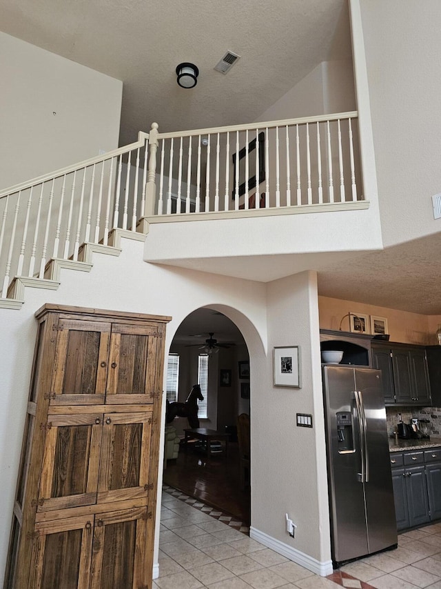 interior space featuring a ceiling fan, arched walkways, a high ceiling, tile patterned flooring, and visible vents