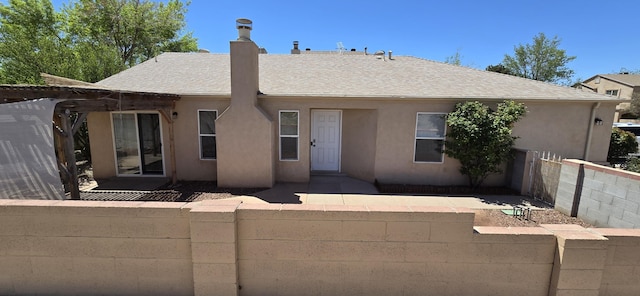 view of front facade featuring a chimney, a shingled roof, and stucco siding