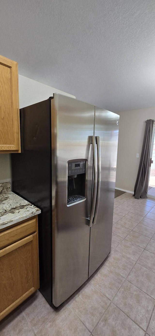 kitchen featuring light tile patterned floors, a textured ceiling, baseboards, light stone countertops, and stainless steel fridge