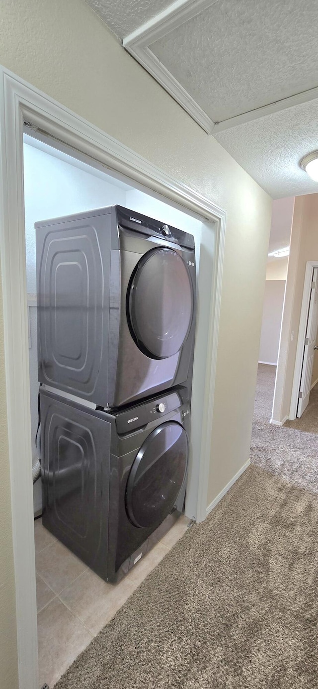 laundry room featuring carpet floors, laundry area, baseboards, stacked washer and clothes dryer, and a textured ceiling
