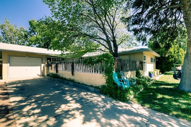 view of side of home featuring a garage, concrete block siding, driveway, and fence