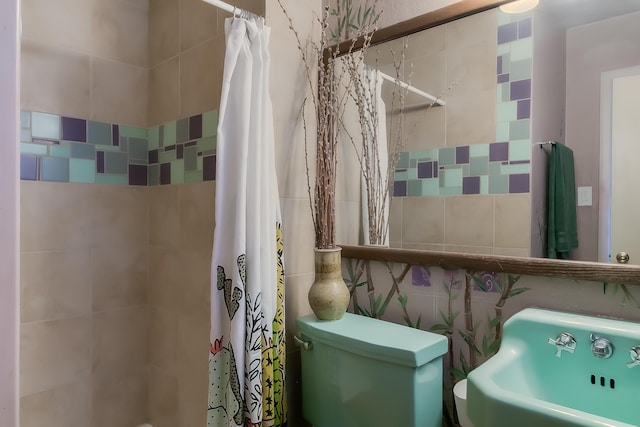 full bath with a tile shower, tile walls, toilet, and a sink