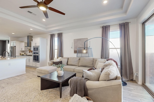 living room featuring ceiling fan, a tray ceiling, light wood finished floors, visible vents, and recessed lighting
