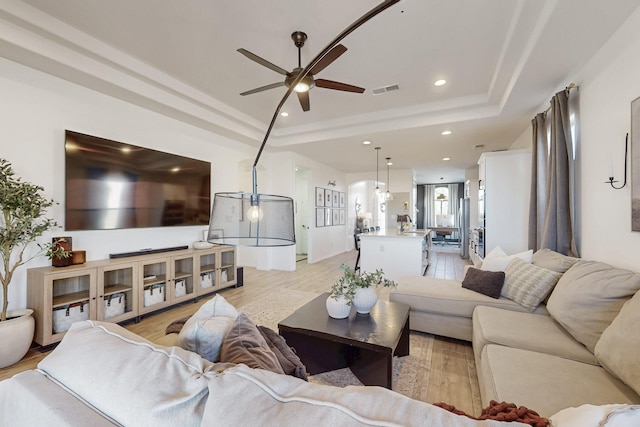 living room with a ceiling fan, light wood-style floors, a raised ceiling, visible vents, and recessed lighting