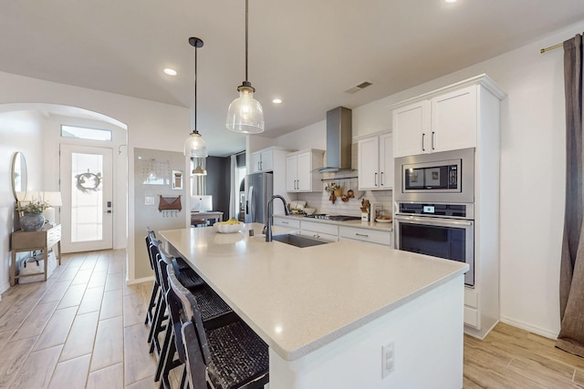 kitchen with stainless steel appliances, a large island, visible vents, a sink, and wall chimney exhaust hood