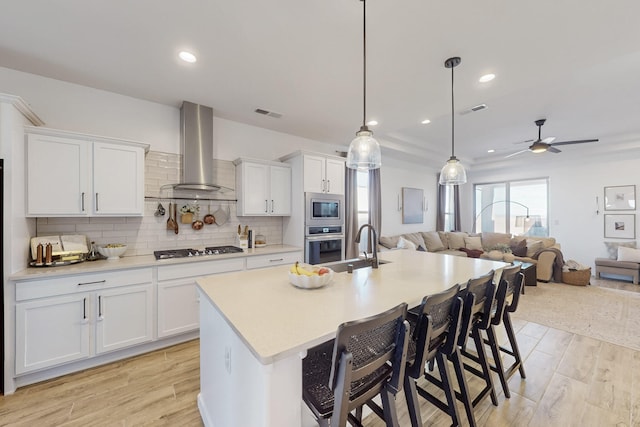 kitchen with wall chimney range hood, stainless steel appliances, light wood-type flooring, and light countertops