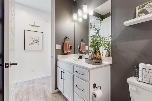 half bath featuring baseboards, wood finished floors, vanity, and toilet
