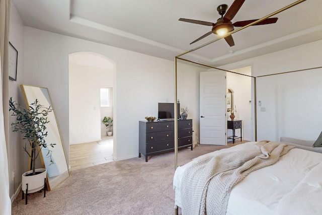 carpeted bedroom with a ceiling fan, a tray ceiling, and arched walkways