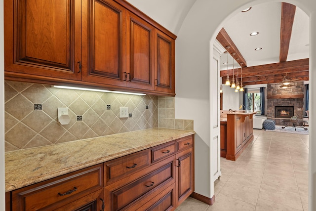 kitchen featuring arched walkways, open floor plan, light stone countertops, a fireplace, and light tile patterned floors