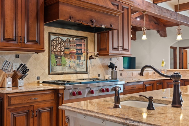 kitchen with stainless steel gas cooktop, tasteful backsplash, beamed ceiling, light stone countertops, and brown cabinetry