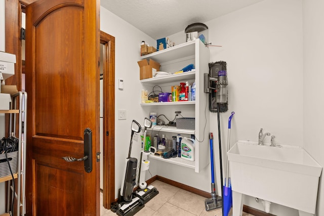 clothes washing area with baseboards, a sink, and light tile patterned floors