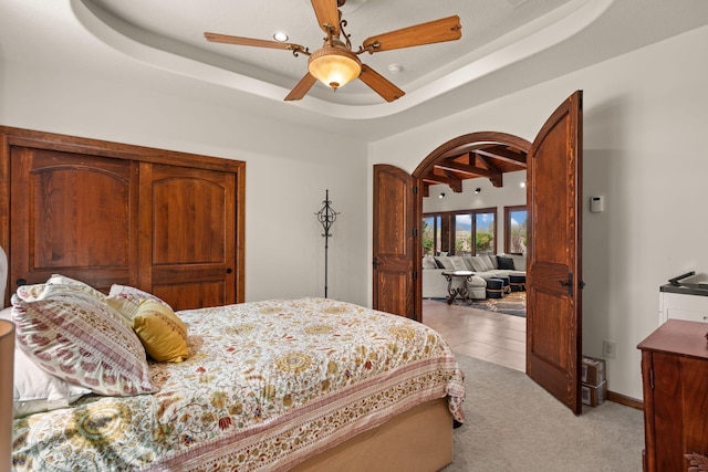 bedroom featuring light carpet, a ceiling fan, a tray ceiling, and arched walkways