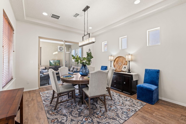dining area featuring baseboards, a tray ceiling, visible vents, and wood finished floors