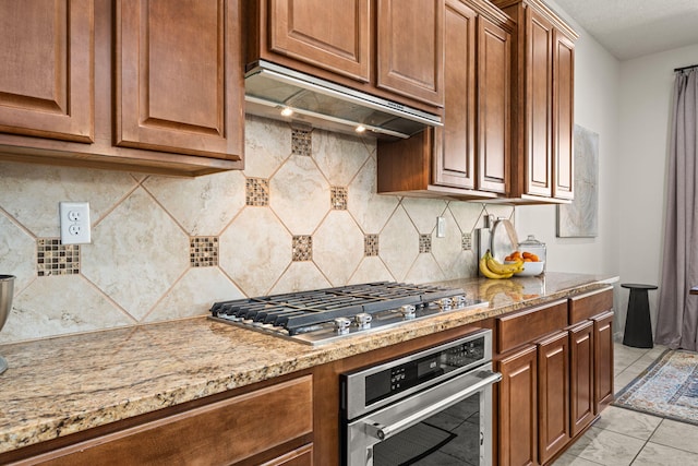 kitchen with decorative backsplash, light stone countertops, stainless steel appliances, and under cabinet range hood