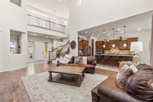 living room featuring stairway, light wood-style floors, recessed lighting, and a towering ceiling