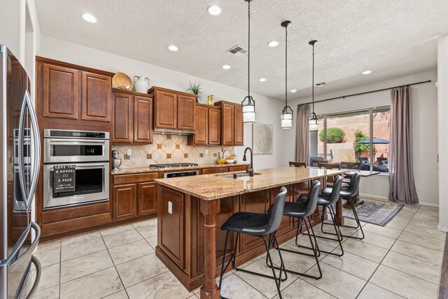 4024 Colina Roja Ln NE, Rio Rancho, NM 87124 - kitchen featuring a sink, appliances with stainless steel finishes, backsplash, an island with sink, and light stone counters
