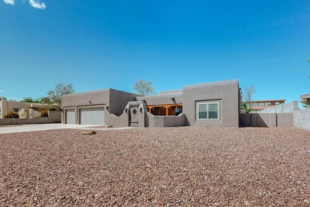 pueblo-style home with stucco siding, a garage, fence, and driveway