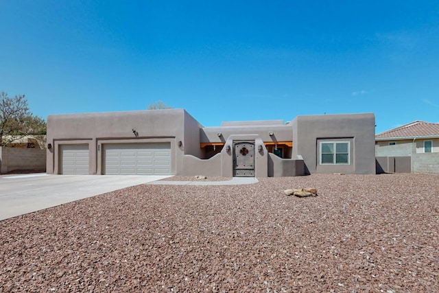 pueblo-style home featuring an attached garage, stucco siding, driveway, and fence