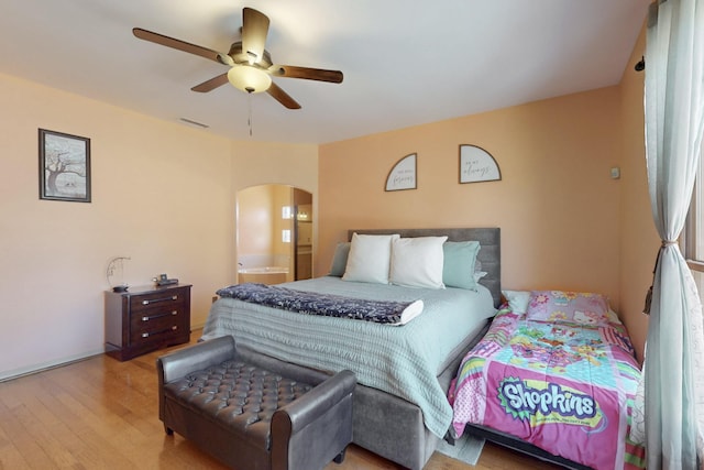 bedroom featuring arched walkways, a ceiling fan, visible vents, and wood finished floors