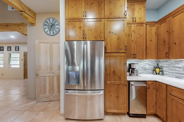 kitchen with backsplash, brown cabinets, light tile patterned floors, light countertops, and stainless steel fridge