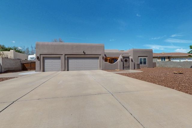 pueblo-style home with fence, stucco siding, an attached garage, and driveway