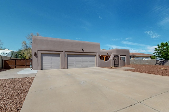 pueblo revival-style home with concrete driveway, a garage, fence, and stucco siding