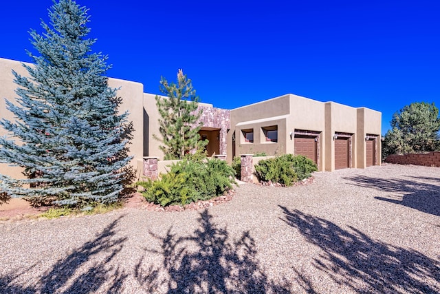 6 Storyteller Ct, Sandia Park, NM 87047 - pueblo-style house featuring stucco siding, an attached garage, and driveway