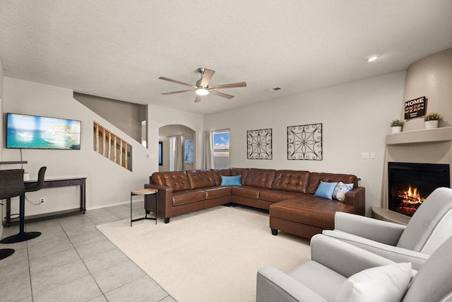 4201 High Mesa Rd SE, Rio Rancho, NM 87124 - living room with light tile patterned floors, arched walkways, a ceiling fan, a lit fireplace, and baseboards