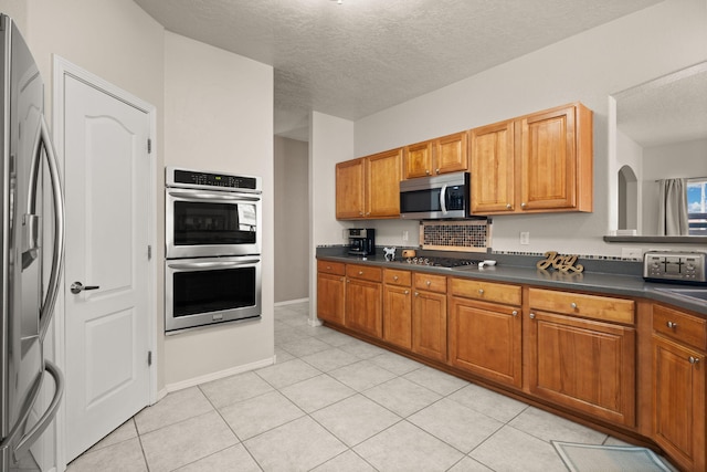 4201 High Mesa Rd SE, Rio Rancho, NM 87124 - kitchen featuring appliances with stainless steel finishes, dark countertops, a textured ceiling, brown cabinets, and light tile patterned floors