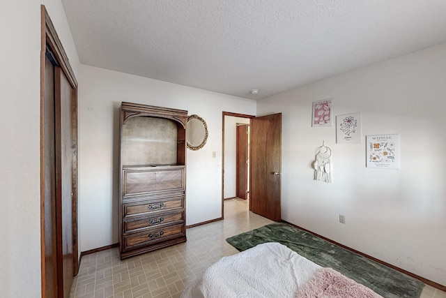 bedroom featuring a textured ceiling, baseboards, and brick patterned floor